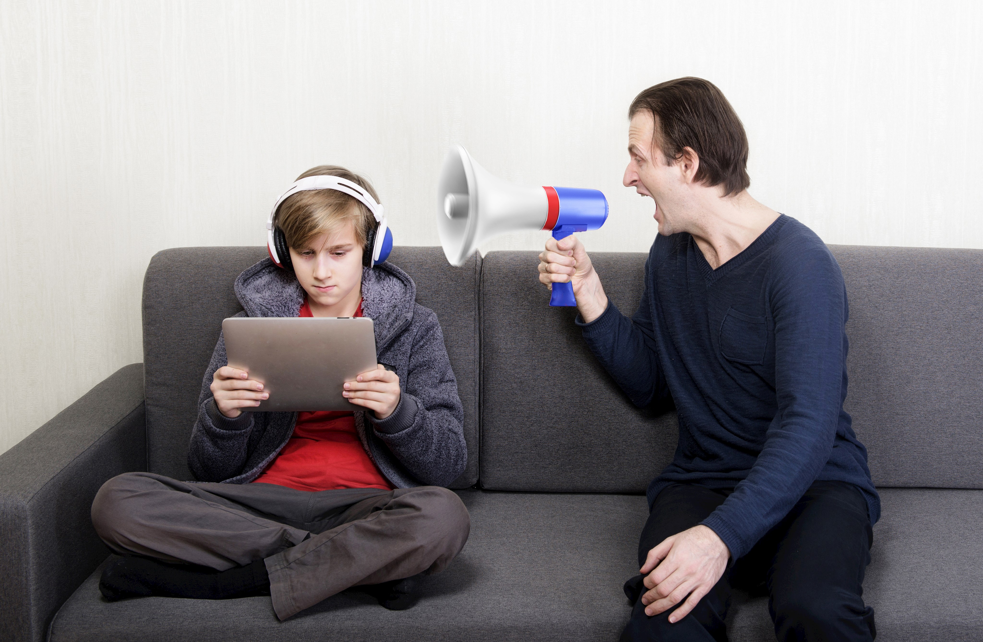 Kind und Vater mit Megaphon sitzen auf der Couch