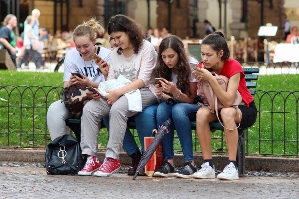 vier Jugendliche sitzen auf einer Bank mit Handy in der Hand