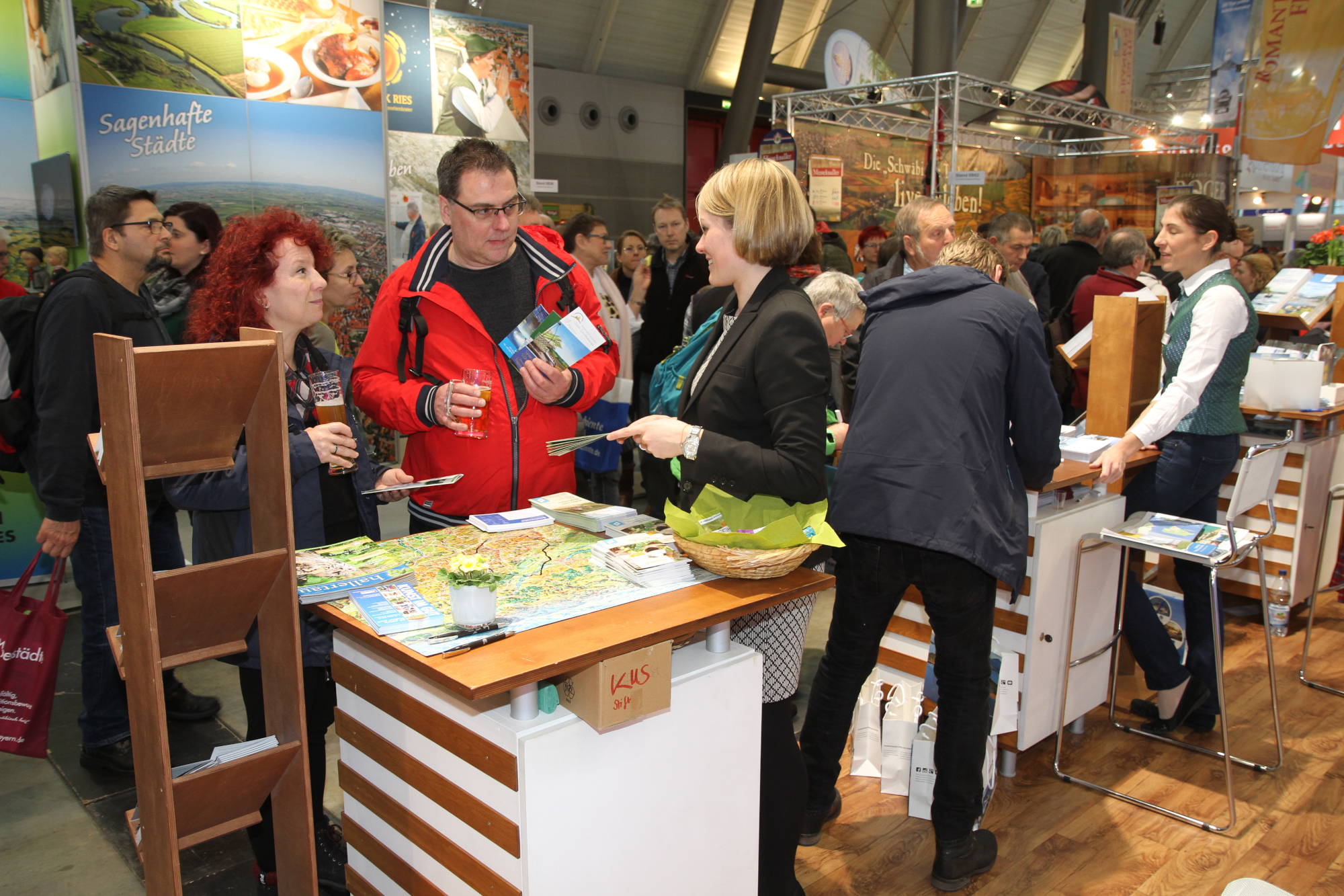 Eine Mitarbeiterin des KUS informiert die interessierten Besucher über die vielfältigen Angebote der Region. Mehrere Personen an einem Messestand
