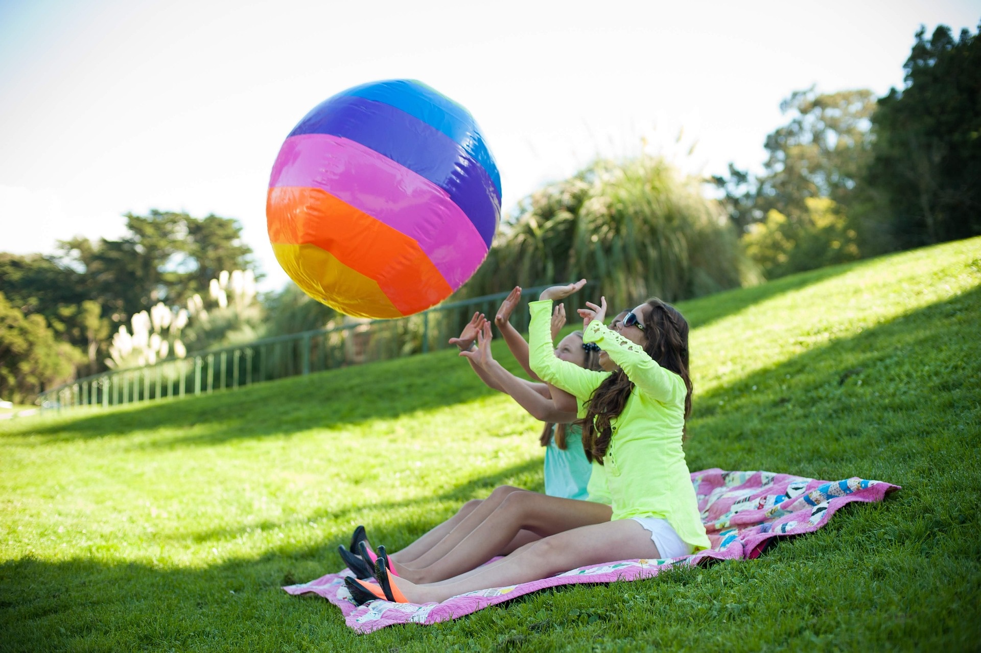 zwei Mädchen sitzen auf Picknickdecke und spielen mit einem Ball