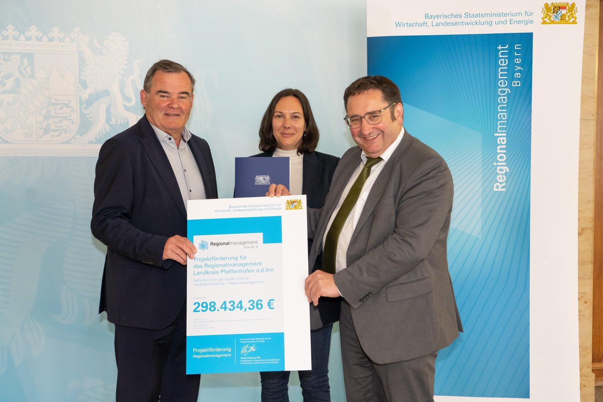 drei Personen stehen nebeneinander und halten eine Urkunde